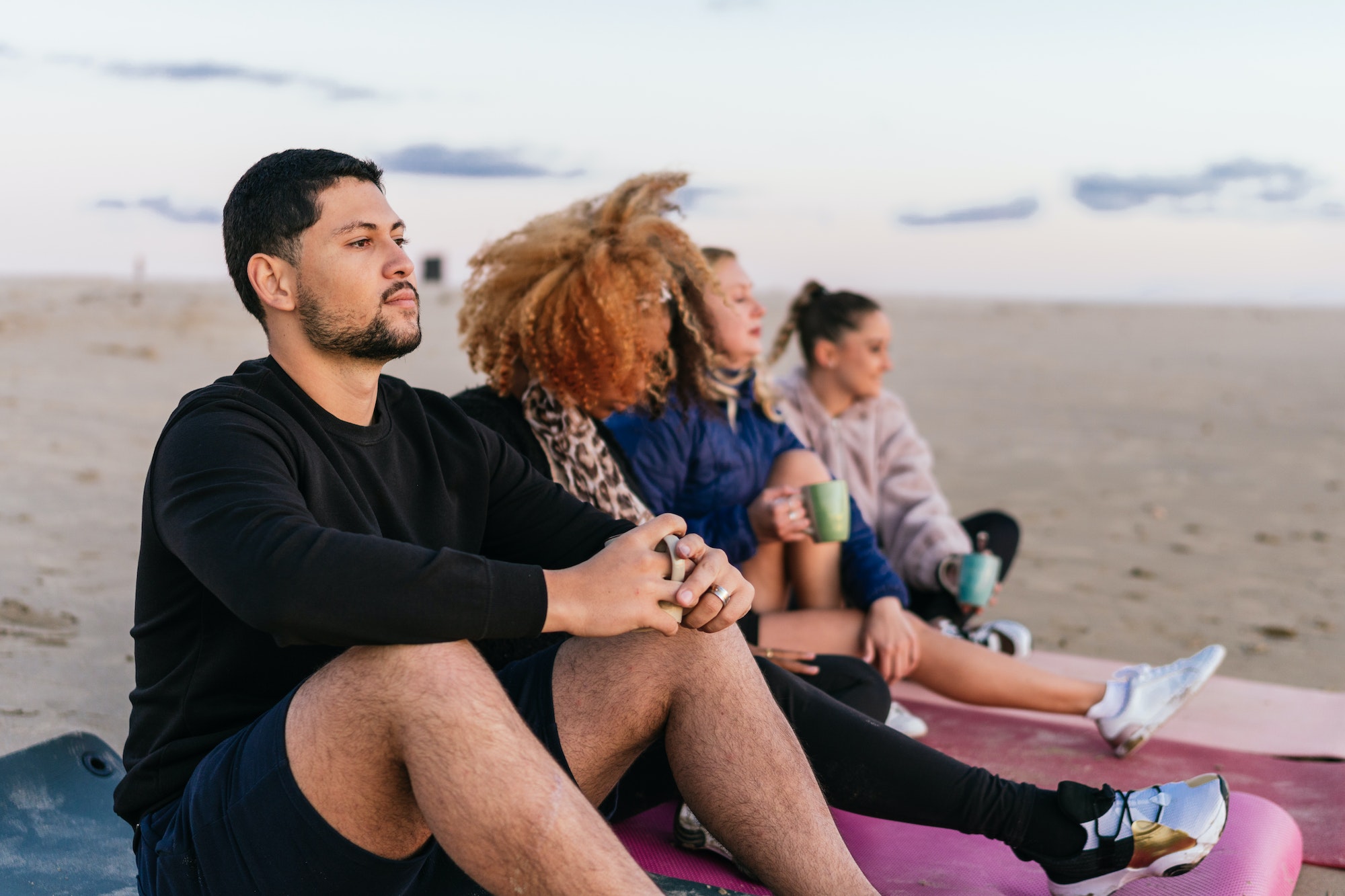 People sitting on mats on the beach drinking tea during the sunset